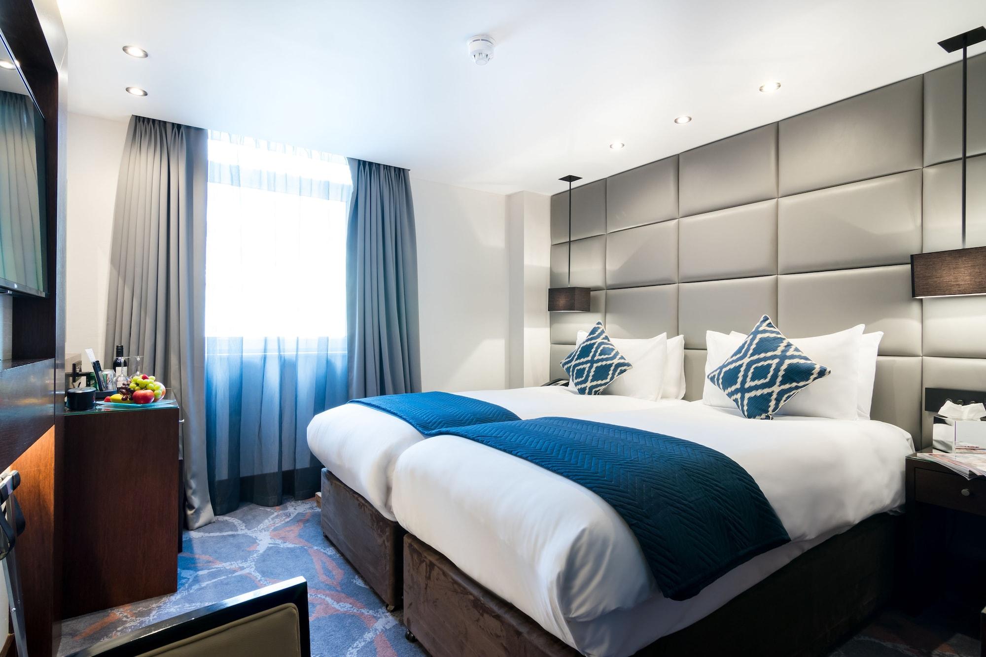 Montcalm Chilworth Townhouse, Paddington Hotell London Eksteriør bilde The image shows a modern hotel room featuring two twin beds with white bedding and blue throws. Each bed has decorative pillows. There are stylish, neutral-colored walls and a large window with sheer curtains allowing natural light to enter. The floo