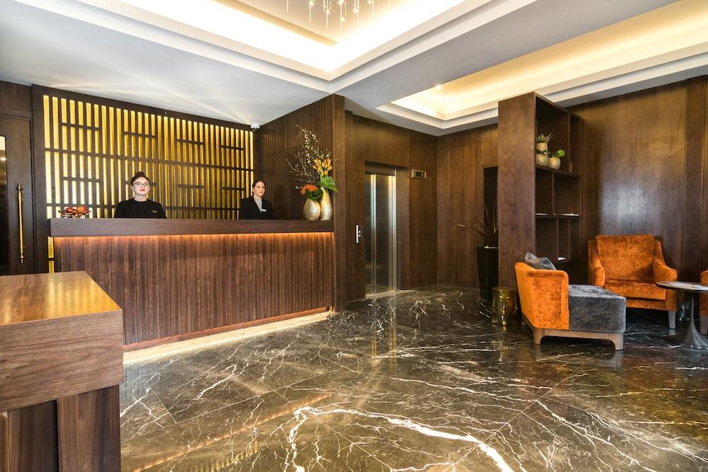 Montcalm Chilworth Townhouse, Paddington Hotell London Eksteriør bilde The photo depicts a modern hotel lobby. In the foreground, there is a reception desk made of dark wood, behind which two staff members are standing. The walls are adorned with a wooden panel design and there are decorative plants and flowers on the d