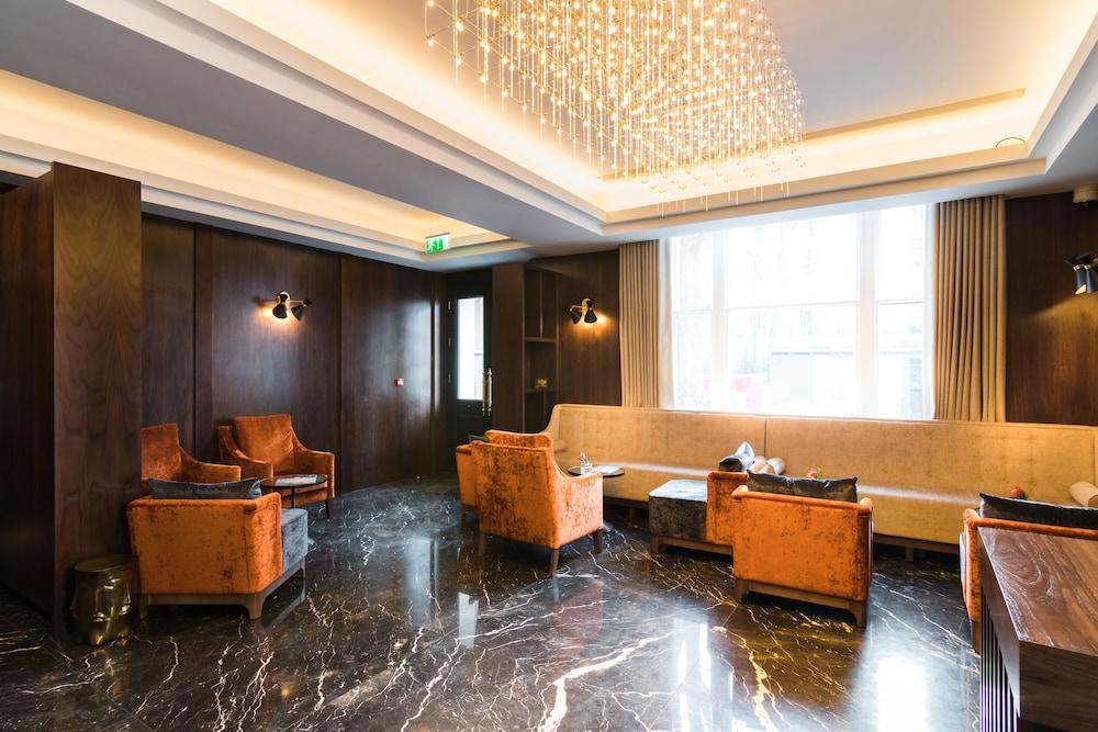 Montcalm Chilworth Townhouse, Paddington Hotell London Eksteriør bilde The photo shows a stylish and modern lounge area. It features dark wooden walls and a polished black marble floor. There are several comfortable armchairs in a warm orange color arranged in the space, accompanied by a long, light-colored sofa. The ce