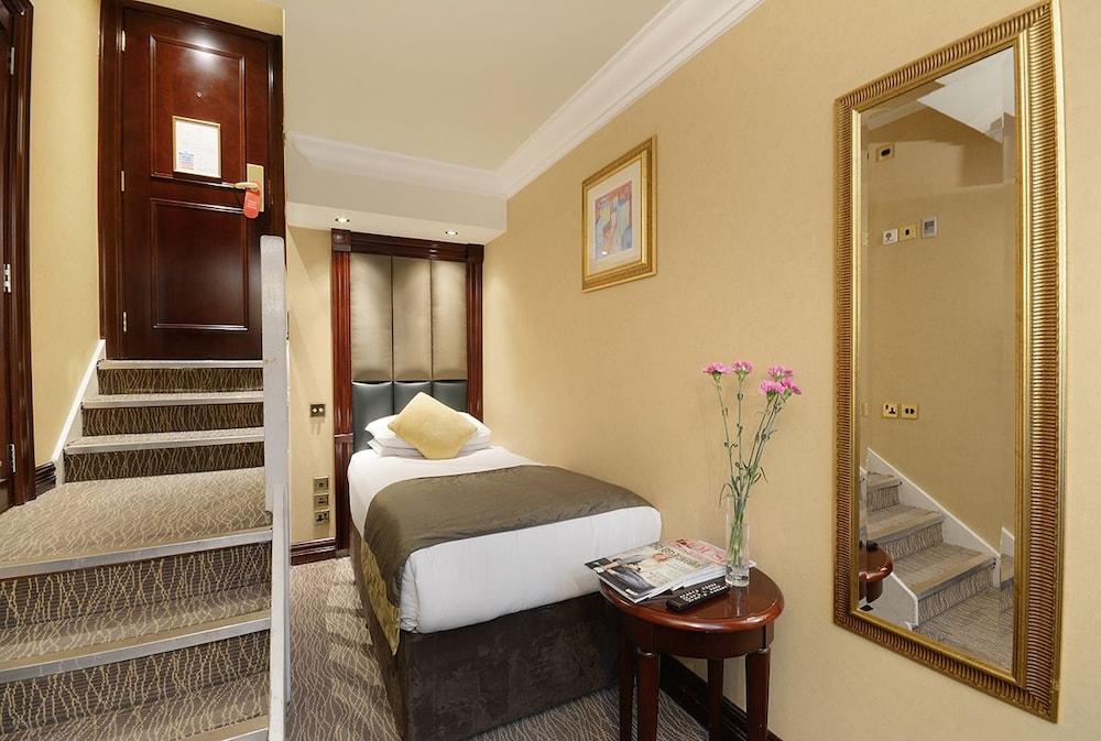 Montcalm Chilworth Townhouse, Paddington Hotell London Eksteriør bilde The photo shows a small hotel room with a cozy atmosphere. On the left, there are stairs leading to another level, while the right side features a bed with a neutral-colored bedspread. A small table beside the bed holds some magazines and a vase with