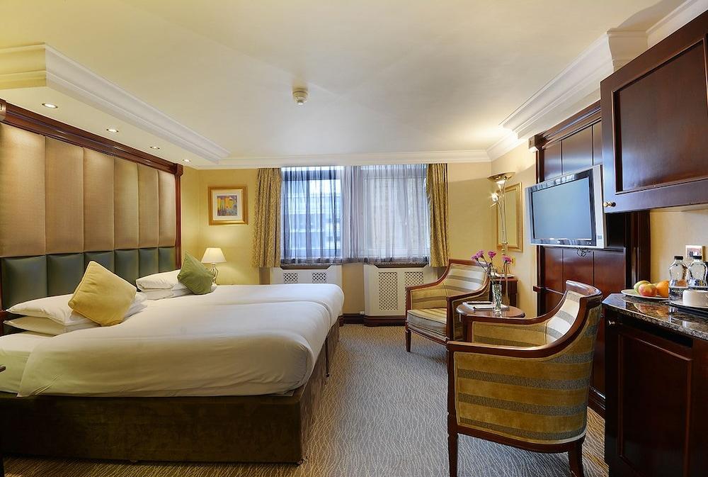Montcalm Chilworth Townhouse, Paddington Hotell London Eksteriør bilde The photo shows a hotel room featuring two single beds with white linens and a decorative pillow on one of them. There are two armchairs in front of a small table, and a flat-screen TV mounted on the wall. The room has large windows with light-colore