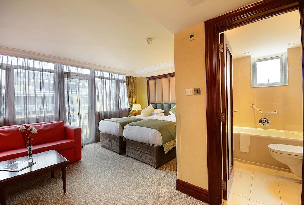 Montcalm Chilworth Townhouse, Paddington Hotell London Eksteriør bilde The photo shows a hotel room featuring two beds with a neutral-colored bedding arrangement. There is a red sofa near a small coffee table, and large windows with sheer curtains allow natural light to fill the space. On the right side, there is a bath