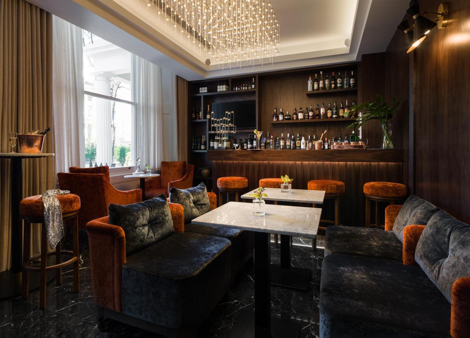 Montcalm Chilworth Townhouse, Paddington Hotell London Eksteriør bilde The photo shows a stylish interior of a bar or lounge area. There are plush seating arrangements with dark, velvet sofas and orange-accented chairs. The tables are marble-topped, and there are decorative elements such as a chandelier hanging from the