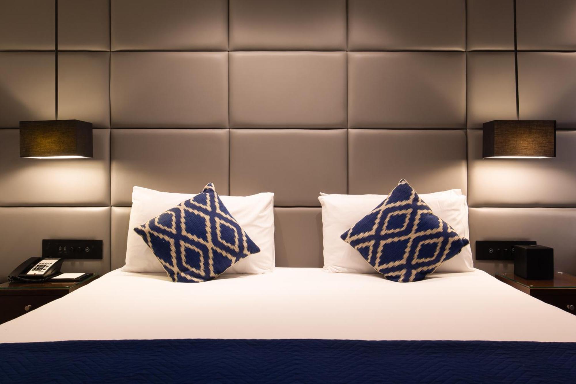 Montcalm Chilworth Townhouse, Paddington Hotell London Eksteriør bilde The photo shows a well-designed hotel room with a neatly made bed. The bed has a white duvet and two decorative pillows with a blue geometric pattern. The headboard is upholstered and features a grid-like design in neutral tones. On either side of th