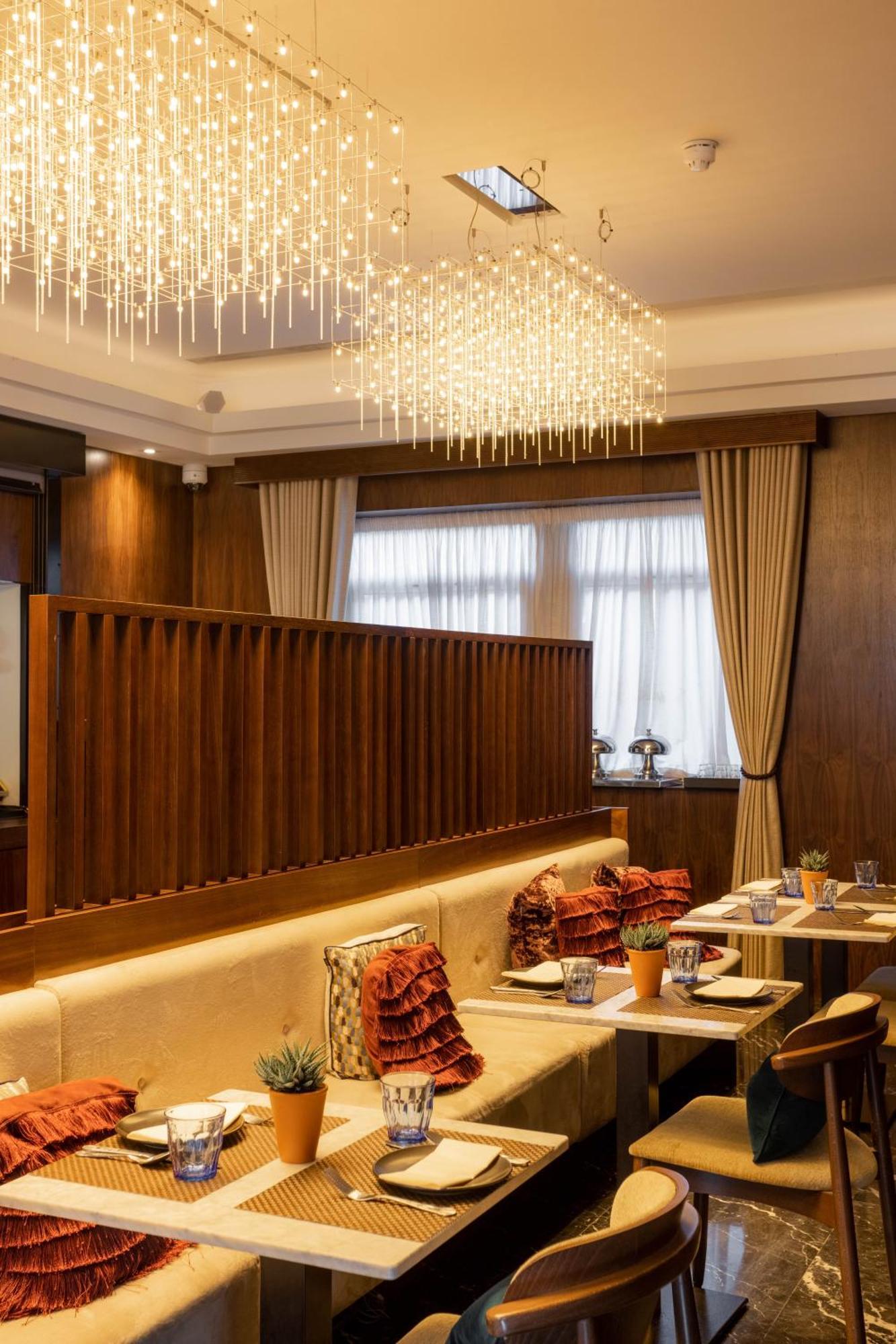 Montcalm Chilworth Townhouse, Paddington Hotell London Eksteriør bilde The photo depicts a stylish restaurant interior. There is a modern chandelier hanging from the ceiling, casting a warm light over the space. The walls are finished in rich wood tones, providing a cozy ambiance. A dividing wall with horizontal slats s