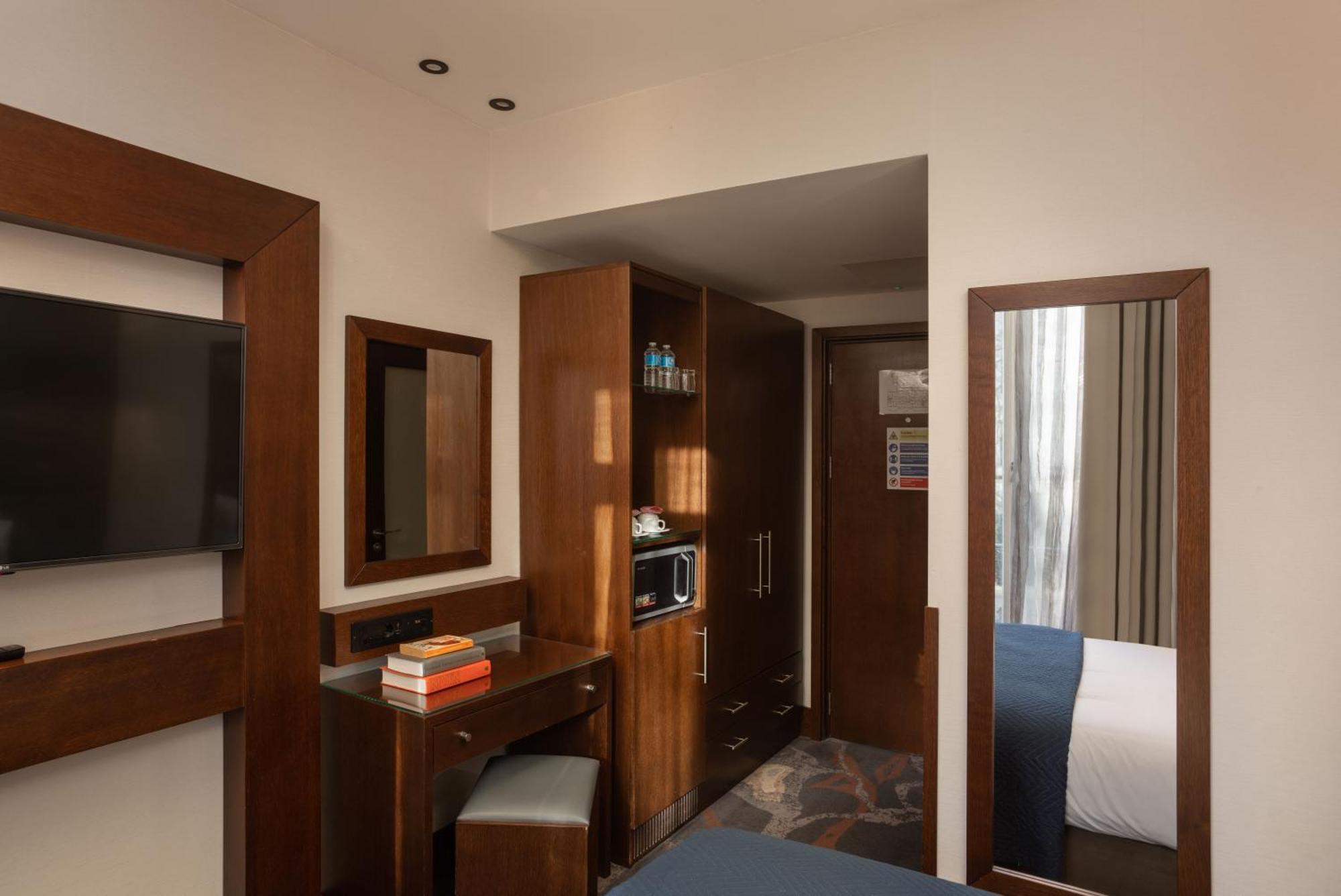 Montcalm Chilworth Townhouse, Paddington Hotell London Eksteriør bilde The photo shows a bedroom with a modern design. It features wooden elements, including cabinets and furniture. There's a flat-screen TV mounted on the wall, a small desk with a chair, and a set of books or items on the desk. A mirrored wardrobe is vi