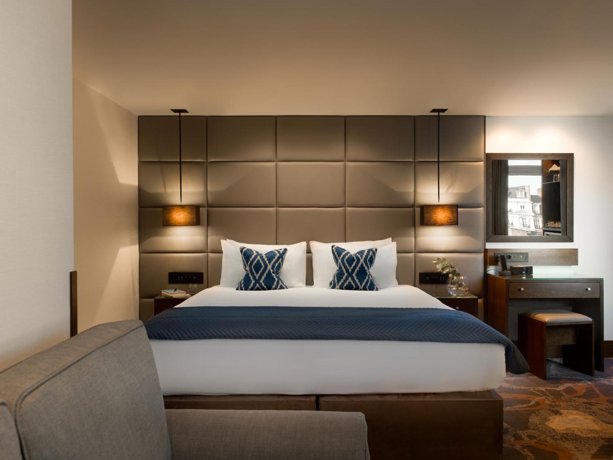 Montcalm Chilworth Townhouse, Paddington Hotell London Eksteriør bilde The photo shows a modern hotel room featuring a neatly made bed with two decorative pillows at the headboard. The headboard itself is upholstered in a grid pattern and flanked by wall-mounted lamps. There's a small desk area to the side with a mirror