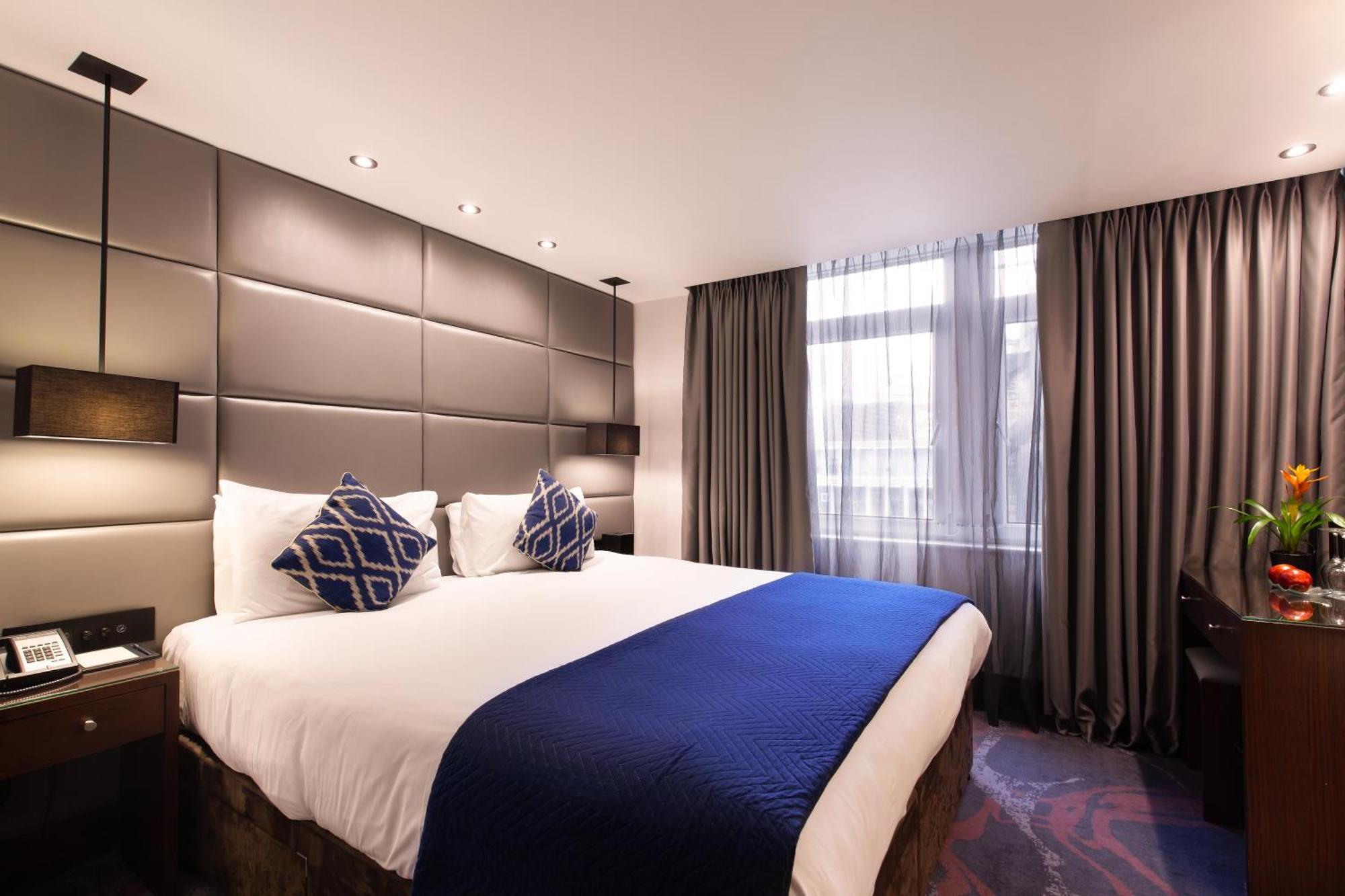 Montcalm Chilworth Townhouse, Paddington Hotell London Eksteriør bilde The photo shows a modern hotel room featuring a large bed with a white and blue color scheme. The bed has decorative cushions, including two blue ones with a geometric pattern. The walls are elegantly designed with a padded panel structure, and there