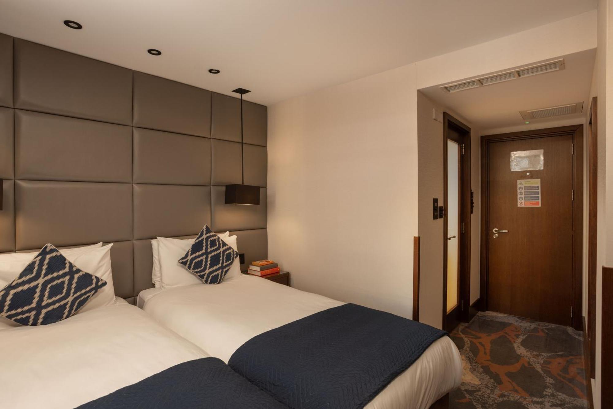 Montcalm Chilworth Townhouse, Paddington Hotell London Eksteriør bilde The photo shows a hotel room featuring two twin beds with dark blue bedspreads. Each bed is adorned with decorative pillows that have a geometric pattern. The headboard of the beds is a padded grey wall, creating a modern and cozy atmosphere. A bedsi