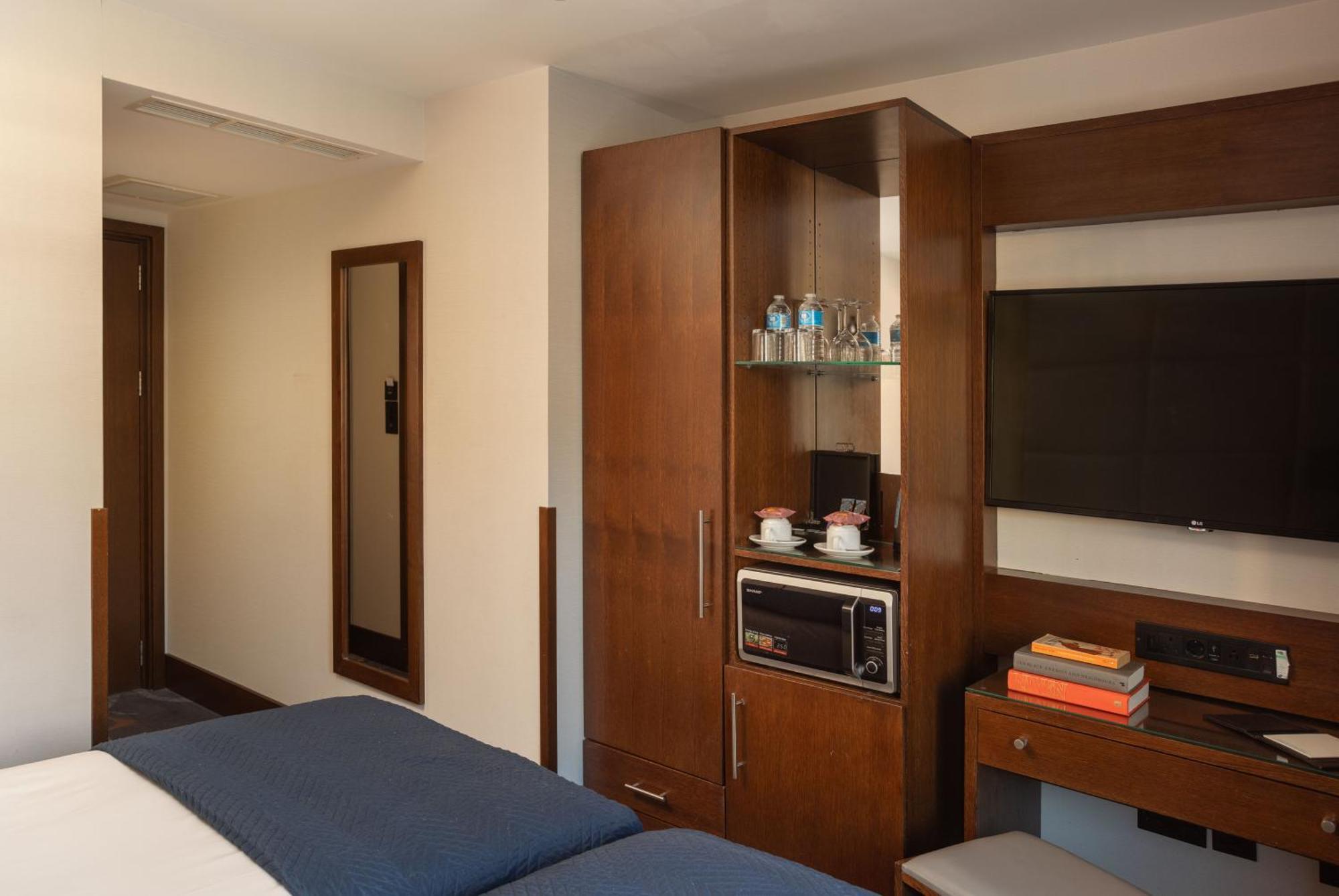 Montcalm Chilworth Townhouse, Paddington Hotell London Eksteriør bilde The photo depicts a hotel room interior featuring two beds with blue bedding. On one side of the room, there is a wooden cabinet that includes a small refrigerator and a television mounted on the wall above it. The cabinet also displays bottles of wa