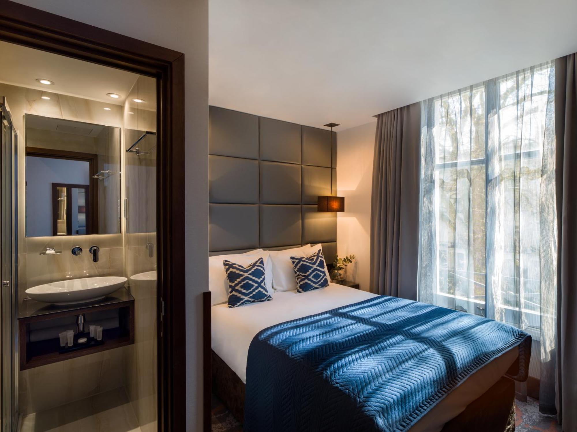 Montcalm Chilworth Townhouse, Paddington Hotell London Eksteriør bilde The photo shows a modern hotel bedroom. It features a neatly made bed with blue and white bedding and two decorative pillows. Beside the bed is a lamp, and large windows allow natural light to fill the space, with sheer curtains draping down. On one 