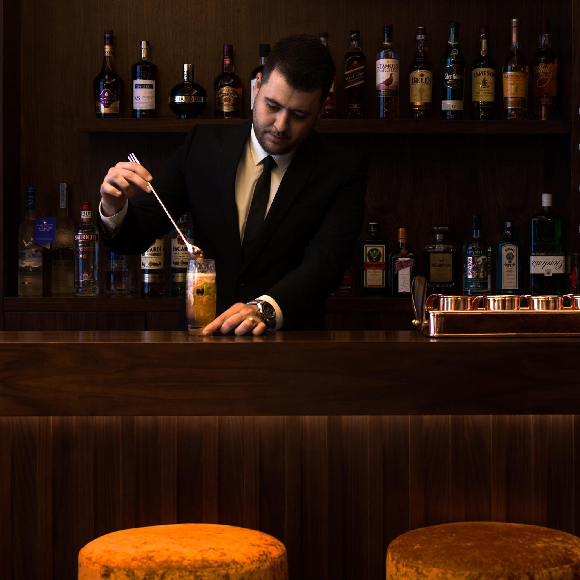 Montcalm Chilworth Townhouse, Paddington Hotell London Eksteriør bilde The image shows a bartender at a bar. He is wearing a black suit and tie and is focused on preparing a cocktail, stirring it with a spoon. Behind him, there is a wooden bar counter and a shelf filled with various bottles of liquor and spirits. The at