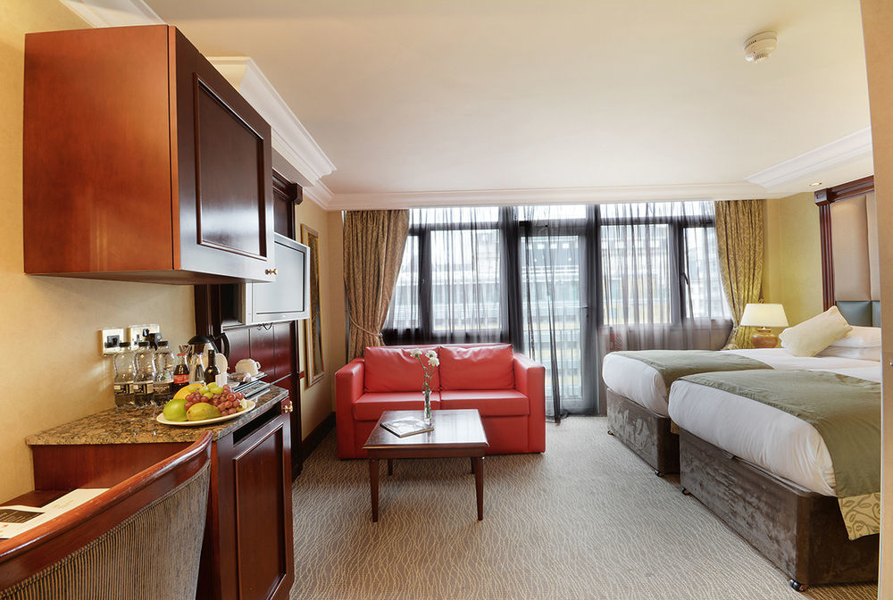 Montcalm Chilworth Townhouse, Paddington Hotell London Eksteriør bilde The photo shows a cozy hotel room featuring two beds with comfortable bedding. There is a red sofa in the sitting area, complemented by a coffee table. Natural light streams in through large windows draped with light curtains, creating a warm atmosph