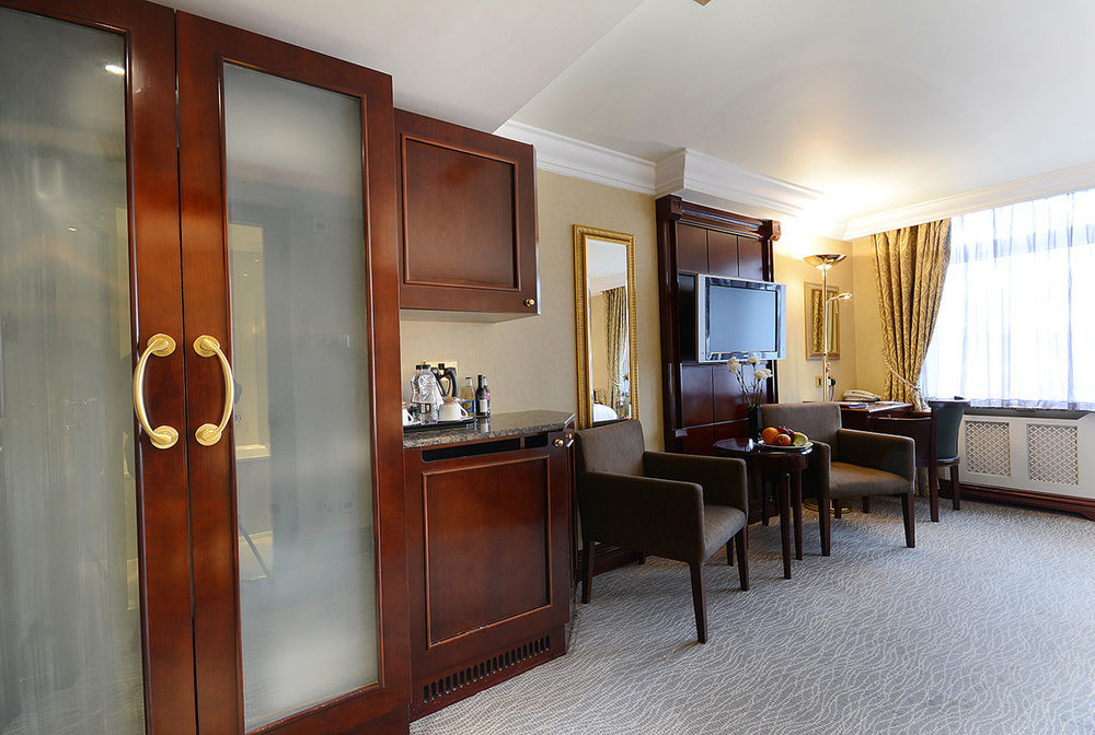 Montcalm Chilworth Townhouse, Paddington Hotell London Eksteriør bilde The photo shows an elegantly designed hotel room with a warm and inviting atmosphere. 

Key features include:

- A wooden cabinet with glass doors, likely providing storage.
- A small bar area with a kettle and coffee-making supplies.
- A mirror and 