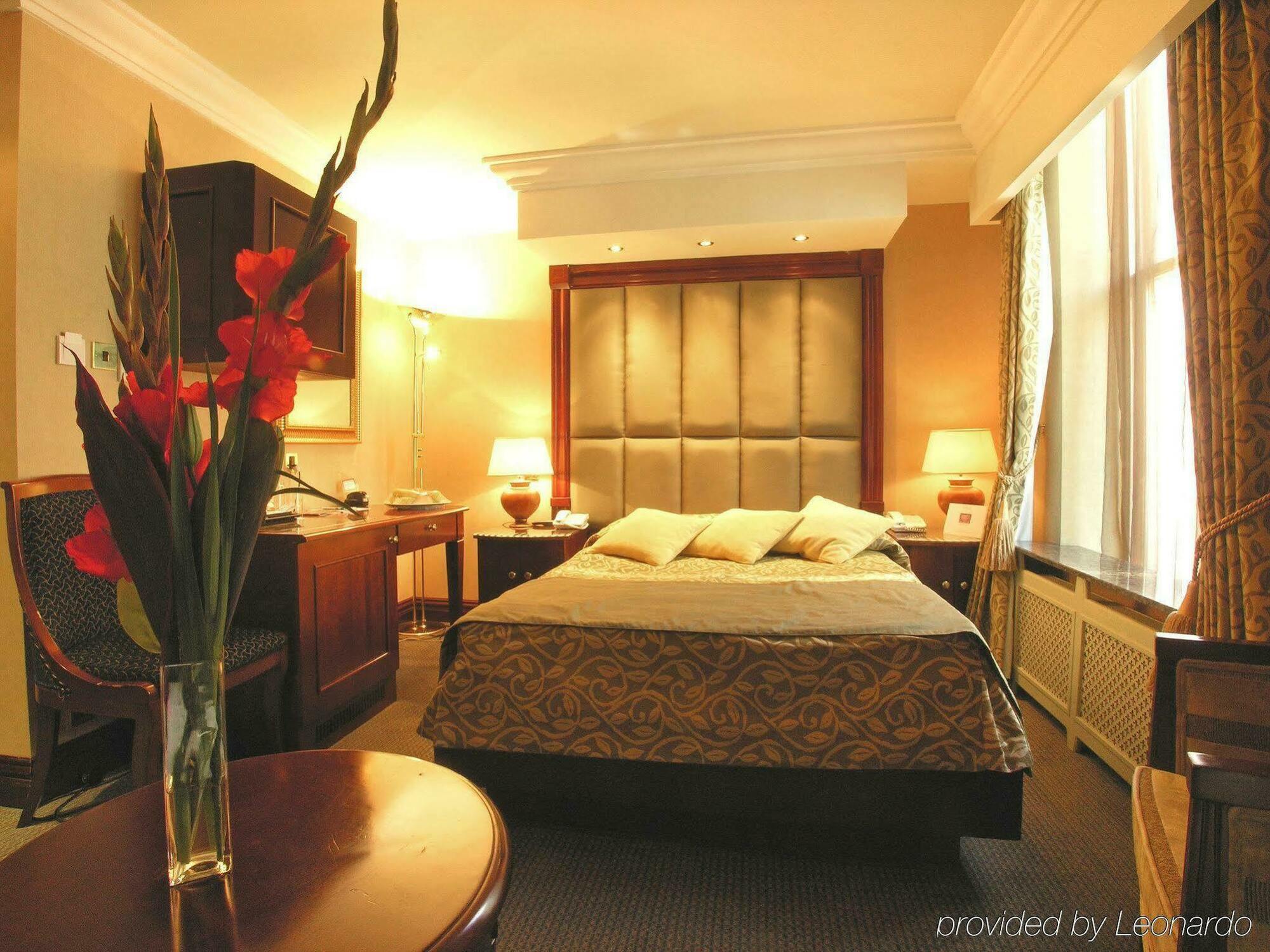 Montcalm Chilworth Townhouse, Paddington Hotell London Rom bilde The photo shows a hotel room that has a cozy and elegant ambiance. The focal point is a large bed with soft pillows and a decorative bedding set. There are bedside lamps on either side of the bed, providing warm lighting. To the left, there is a wood