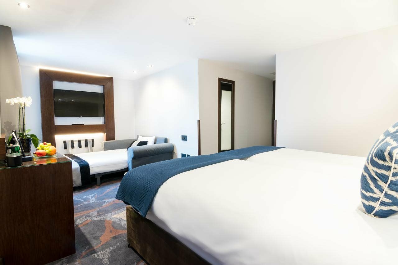 Montcalm Chilworth Townhouse, Paddington Hotell London Eksteriør bilde The photo shows a modern hotel room featuring a large bed with white bedding and a blue accent blanket. On one side of the bed, there is a contemporary-style chair, and in the background, there is a smaller sofa or daybed. A stylish area rug covers t